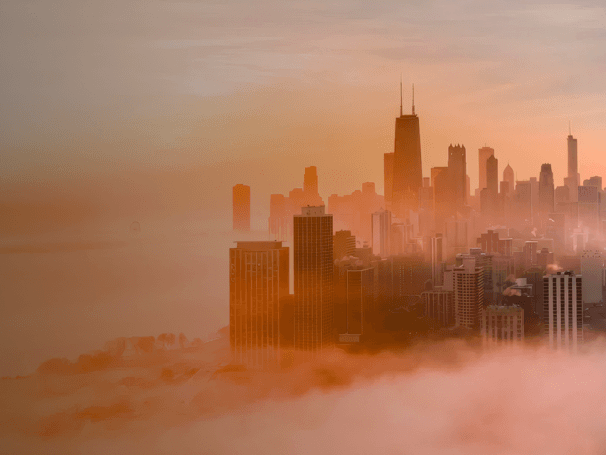 Stadtansicht mit Hochhäusern, die aus dichtem Nebel ragen, beleuchtet vom Sonnenaufgang oder Sonnenuntergang