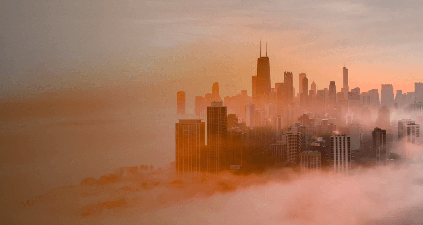Stadtansicht mit Hochhäusern, die aus dichtem Nebel ragen, beleuchtet vom Sonnenaufgang oder Sonnenuntergang