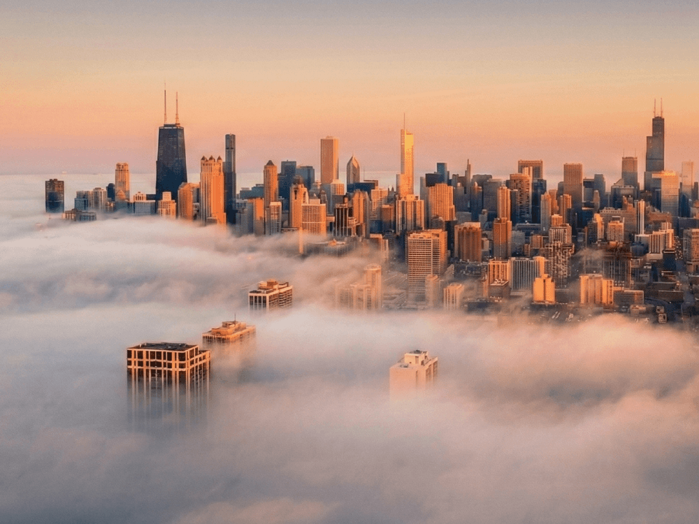 Hochh&auml;user, die aus dichtem Nebel ragen, beleuchtet vom warmen Morgenlicht