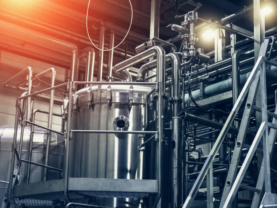 Industrielle Anlage mit großem zylindrischem Edelstahltank, umgeben von Rohrleitungen und Metalltreppen