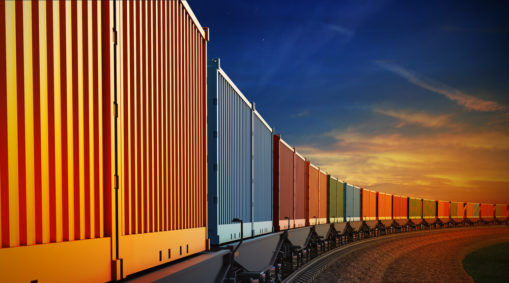 Lange Reihe bunter Gütercontainer auf Eisenbahnwaggons vor einem Abendhimmel