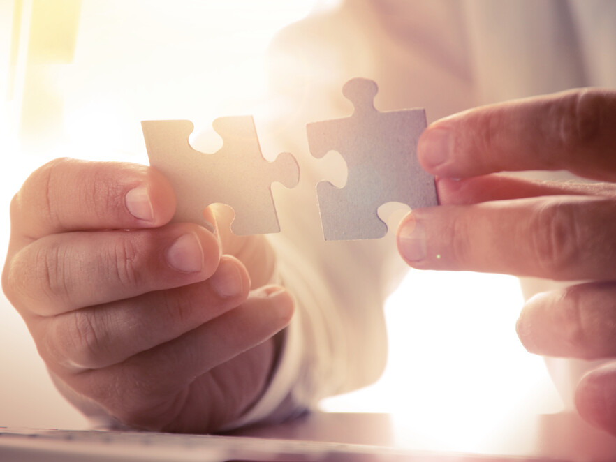 Hände halten zwei Puzzleteile vor hellem Hintergrund