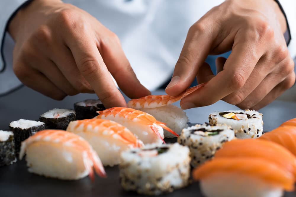 H&auml;nde legen Garnelen-Sushi auf eine Platte mit einer Auswahl verschiedener Sushiarten